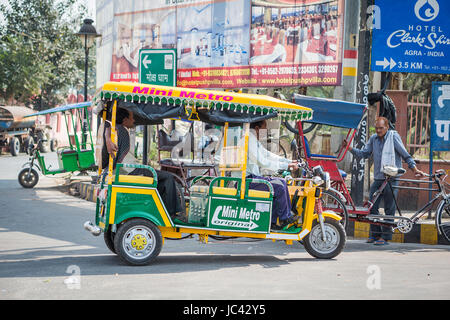 Ein neuen gelben und grünen motorisierten Tuk-Tuk transportiert ein Kunde vorbei an mehreren parkenden Rikschas an einer Straßenecke in Agra, Uttar Pradesh, Indien Stockfoto