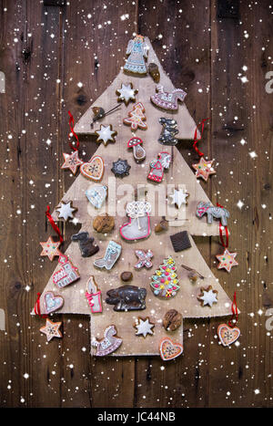 Handgemachte geschnitzte Weihnachtsbaum dekoriert mit Lebkuchen, Sternen und Herzen auf hölzernen Hintergrund. Stockfoto