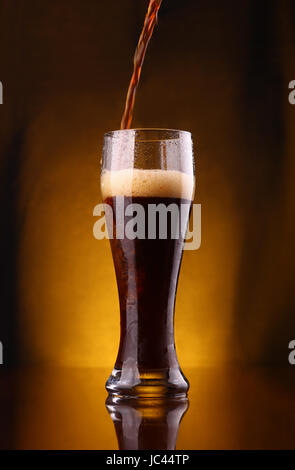 Dunkles Bier eingießen in ein hohes Glas aus einer Flasche Stockfoto