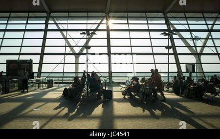 Passagiere in Silhouette in der sonnendurchfluteten Abfluggate für den Flug am frühen Morgen warten, Shanghai Pudong International Airport, China Stockfoto