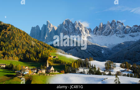 Zusammengesetztes Bild von zwei Fotos, die zwei Tage nach einander zeigen die Veränderung der Saison Herbst-Winter. Das Dorf St. Magdalena oder Santa Maddalena mit Kirche vor den Geisler Dolomiten Gipfeln in der Val di Funes in Italien. Stockfoto