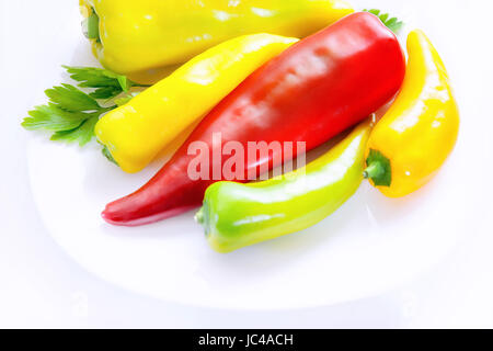 Weiße Schale mit Paprika in verschiedenen Größen und Farben. Rot, grün und gelb ganze. Rohes Gemüse. Langer Pfeffer. Stockfoto