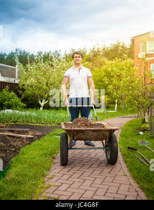 Gut aussehender Mann mit Schubkarre im schönen Garten Stockfoto