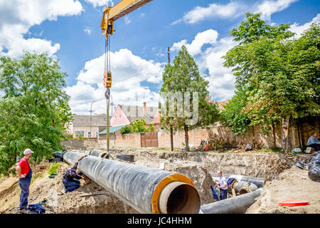 Kranhaken mit Trägern ist das riesige lange Rohr über staubigen Boden ziehen. Stockfoto