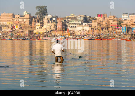 Ein Fischer ist mit einem Netz auf den Sandbänken am heiligen Fluss Ganges, Panorama der dashashwamedh Ghat, main Ghat, in der Ferne Stockfoto