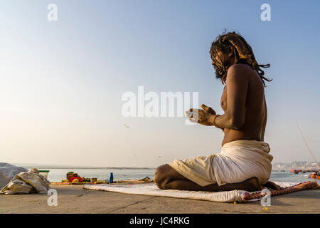 Ein sadhu, heiliger Mann, sitzt und Beten auf einer Plattform am heiligen Fluss Ganges Meer Ghat im Vorort godowlia Stockfoto