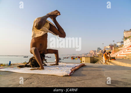Ein sadhu, heiliger Mann, ist das Üben von Yoga Asana auf einer Plattform am heiligen Fluss Ganges Meer Ghat im Vorort godowlia Stockfoto