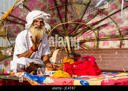 Ein sadhu, heiliger Mann, sitzt unter einem Sonnenschirm am heiligen Fluss Ganges dashashwamedh Ghat, main Ghat, in der Vorstadt godowlia Stockfoto