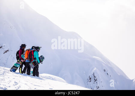 Professionelle Snowboarder Jamie Anderson, Robin Van Gyn und Helen Schettini stehen auf einem Bergrücken und schaue hinunter auf eine Zeile, die sie an einem sonnigen Tag in Haines, Alaska fahren sollen. Stockfoto