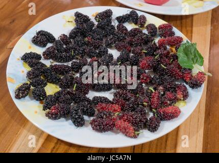 Frische Früchte, Delicious und süßen Maulbeeren mit grünen Blättern in White Plate auf A Holztisch. Stockfoto