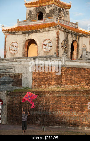 Ein vietnamesischer junge fliegt seinen Kite vor einem Turm im kaiserlichen Gehäuse der Zitadelle, in der alte, historische Stadt Hue, heute ein UNESCO-Weltkulturerbe für seine Architektur und historische Bedeutung. Hue ist seit langem politisch und kulturell das Zentrum von Vietnam und hält jetzt ein beliebtes touristisches. Stockfoto