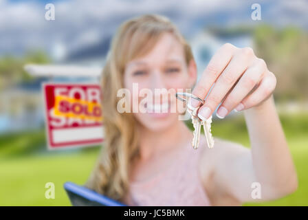 Erregte Frau hält Hausschlüssel und verkauft Immobilien Schild vor schönes neues zu Hause. Stockfoto