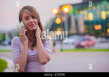 Glückliches Mädchen mit einem Smartphone in einem Stadtpark. Porträt der glückliche junge Frau mit Smartphone in den Händen Stockfoto