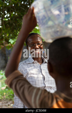 Wasser auf dem Kopf tragen junge wird von einer Frau, Nigeria, Afrika begrüßt. Stockfoto