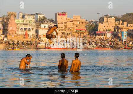 Die jungen Männer haben Spaß und springen Sie auf den Sandbänken am heiligen Fluss Ganges, Panorama der Dashashwamedh Ghat, Main Ghat, in der Ferne Stockfoto