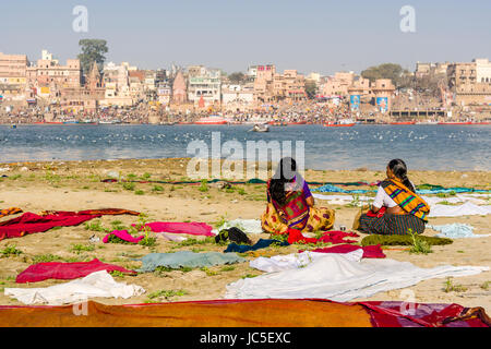 Zwei Frauen sitzen auf den Sandbänken am heiligen Fluss Ganges, warten auf ihre Wäsche zu trocknen, Panorama der dashashwamedh Ghat, main Ghat, in der Stockfoto
