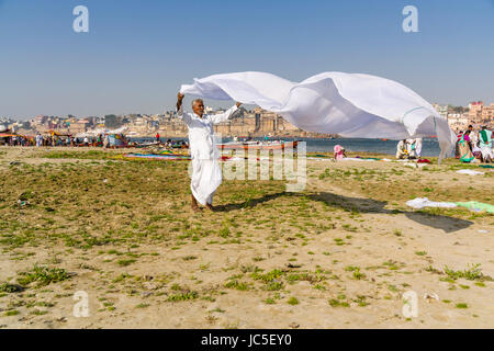 Ein Mann seine Wäsche trocknen im Wind auf den Sandbänken am heiligen Fluss Ganges, Panorama der dashashwamedh Ghat, main Ghat, in der Ferne Stockfoto