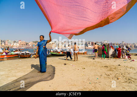 Eine Frau ist das Trocknen ihrer Sari im Wind auf den Sandbänken am heiligen Fluss Ganges, Panorama der dashashwamedh Ghat, main Ghat, in der Ferne Stockfoto