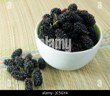 Frisches Obst, süße und Reife Maulbeeren in einer weißen Schüssel auf Strohmatte Stockfoto