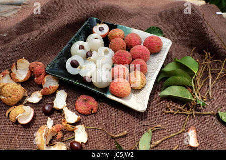 Obstteller auf braunem Hintergrund, Litschi oder Lychee Früchte oder Vai Thieu hautnah. Rote Früchte schälen mit saftigen Fruchtfleisch in weiß, süß und lecker Stockfoto