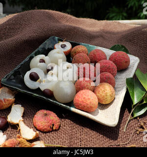 Obstteller auf braunem Hintergrund, Litschi oder Lychee Früchte oder Vai Thieu hautnah. Rote Früchte schälen mit saftigen Fruchtfleisch in weiß, süß und lecker Stockfoto