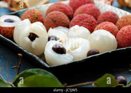 Obstteller auf blauem Hintergrund, Litschi oder Lychee Früchte oder Vai Thieu hautnah. Rote Früchte schälen mit saftigen Fruchtfleisch in weiß, süß und lecker Stockfoto