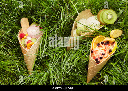 Drei verschiedenen aromatischen Eis mit Waffel Kegel mit frischen Beeren und Früchten, Kiwi, Orange, Banane, Himbeeren auf einem Hintergrund von grünen Rasen f Stockfoto