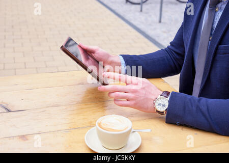 Ernte-Schuss von Business Mannhände neben einer Tasse Kaffee mit Tablet beim Sitzen am Tisch draußen Stockfoto