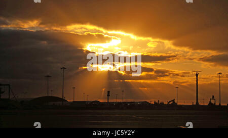 Sonne bricht durch die Wolken bei Sonnenuntergang über einem Flugplatz Stockfoto