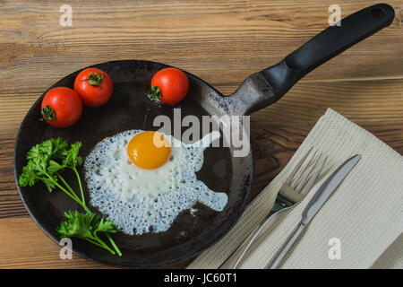 Spiegelei mit Petersilie grün, Tomaten in der Pfanne mit Serviette, Messer und Gabel. Gesundes Frühstück Stockfoto