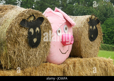 Comic-Tiergesichtern Vertretung Schafe und ein rosa Schwein schmücken drei Heuballen, angeordnet in einem Feld in der Nähe von Dorchester. Dorset, England, Vereinigtes Königreich. Stockfoto