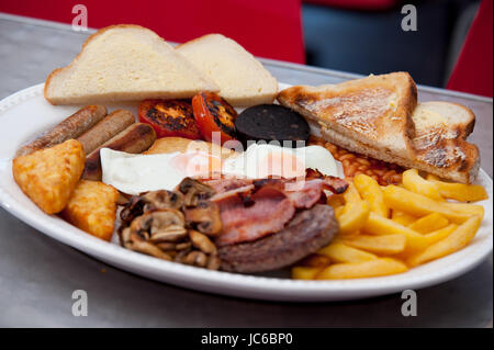 Ein riesiges Frühstück. Bestehend aus 2 Eiern, 3 Speck, 3 Würstchen, Pommes frites, Rösti, Bohnen, Tomaten, Pilze, Burger, gebutterte Scheibe Toast. Stockfoto