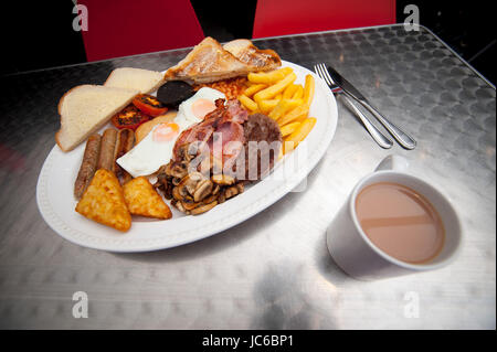 Ein riesiges Frühstück. Bestehend aus 2 Eiern, 3 Speck, 3 Würstchen, Pommes frites, Rösti, Bohnen, Tomaten, Pilze, Burger, gebutterte Scheibe Toast. Stockfoto