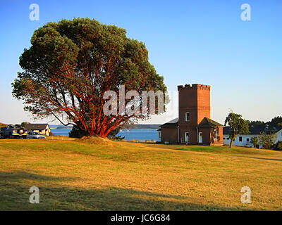 Ein Foto von einem alten militärischen Gebäude in der Nähe einer Wasserstraße.  Der große Baum auf dem Bild ist eine pazifische Madrone Baum.  Die Pazifische Madrone (lateinischer Name: Arbutus Menziesii) ist eine Baumart fand an der Westküste von Nordamerika.  Es ist bekannt für seinen unverwechselbaren roten abblätternde Rinde. Stockfoto