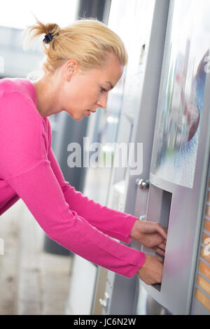 Hübsche junge Mädchen tragen rosa Top Produkt aus einem Vending-Automaten zu sammeln. Stockfoto