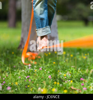 Guy üben Slackline im Stadtpark. Slacklinen ist eine Praxis in der Balance, die in der Regel, Nylon oder Polyester Gurtband zwischen zwei Ankerpunkten gespannt verwendet. Stockfoto