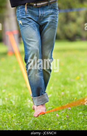 Guy üben Slackline im Stadtpark. Slacklinen ist eine Praxis in der Balance, die in der Regel, Nylon oder Polyester Gurtband zwischen zwei Ankerpunkten gespannt verwendet. Stockfoto