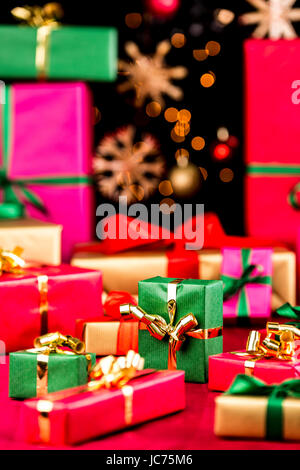 Viele einfache Weihnachtsgeschenke auf einem roten Tuch angeordnet. Engen Schärfentiefe. Vor allem weiche Formen in leuchtenden Farben. Defokussierten Stroh Sterne und Kugeln auf schwarzem Hintergrund. Konzentrieren Sie sich auf zentrale Greenbox. Stockfoto