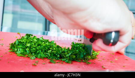 Männlichen Chef schneiden Petersilie mit großen Messer auf Schneidebrett rot Stockfoto