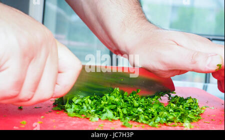 Männlichen Chef schneiden Petersilie mit großen Messer auf Schneidebrett rot Stockfoto