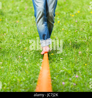 Guy üben Slackline im Stadtpark. Slacklinen ist eine Praxis in der Balance, die in der Regel, Nylon oder Polyester Gurtband zwischen zwei Ankerpunkten gespannt verwendet. Stockfoto