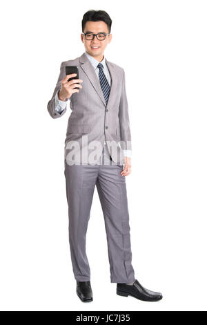 Ganzkörper von jungen asiatischen Geschäftsmann mit Smartphone, SMS und Blick auf das Telefon mit einem Lächeln auf seinem Gesicht, isoliert auf weißem Hintergrund. Stockfoto