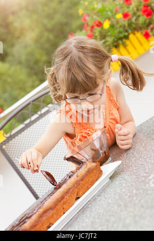 Kleines Mädchen Beim Schokoladenkuchen verzieren Stockfoto