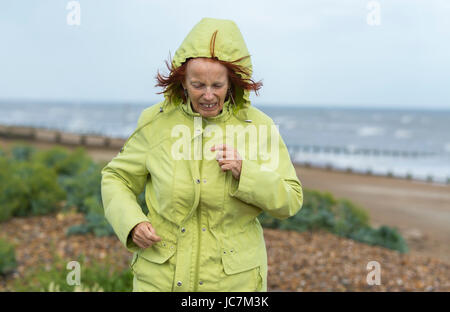 Frau mittleren Alters, die auf einem Strand in kaltem Wetter in einem Mantel bekleidet warm zu halten, an trüben Tagen in Großbritannien. Stockfoto