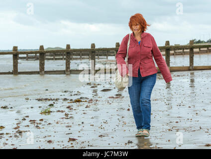 Ältere aber jünger aussehende Frau zu Fuß am Strand bei Ebbe, aktiv zu bleiben. Senior aktiv bleiben. Stockfoto