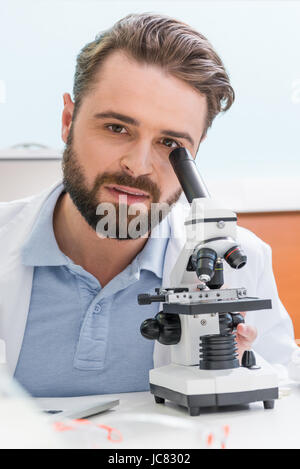bärtige Wissenschaftler arbeiten mit Mikroskop und Blick in die Kamera im Labor Stockfoto