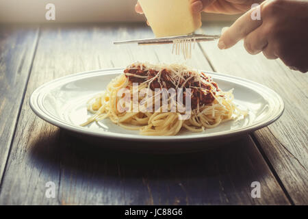Frisch gekochte Spaghetti Bolognese auf einem weißen Teller und mit weiblichen Händen reiben von Parmesan-Käse Stockfoto