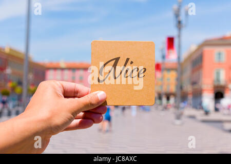 Nahaufnahme eines kaukasischen Jünglings mit einem braunen Schild mit dem Wort Nizza geschrieben vor dem berühmten Place Massena Platz in Nizza, Franken Stockfoto