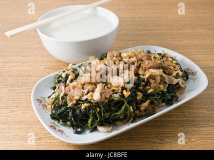 Chinesische traditionelle Speisen, Stir Fried Jute lässt oder Mulukhiyah Blätter mit gehacktem Schweinefleisch, Knoblauch und fermentierte Soja Bohnen serviert mit Reisbrei. Stockfoto