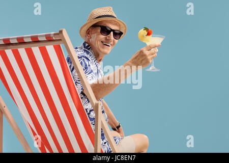 Ältere Touristen mit einem cocktail sitzt auf einem Liegestuhl auf blauem Hintergrund isoliert Stockfoto